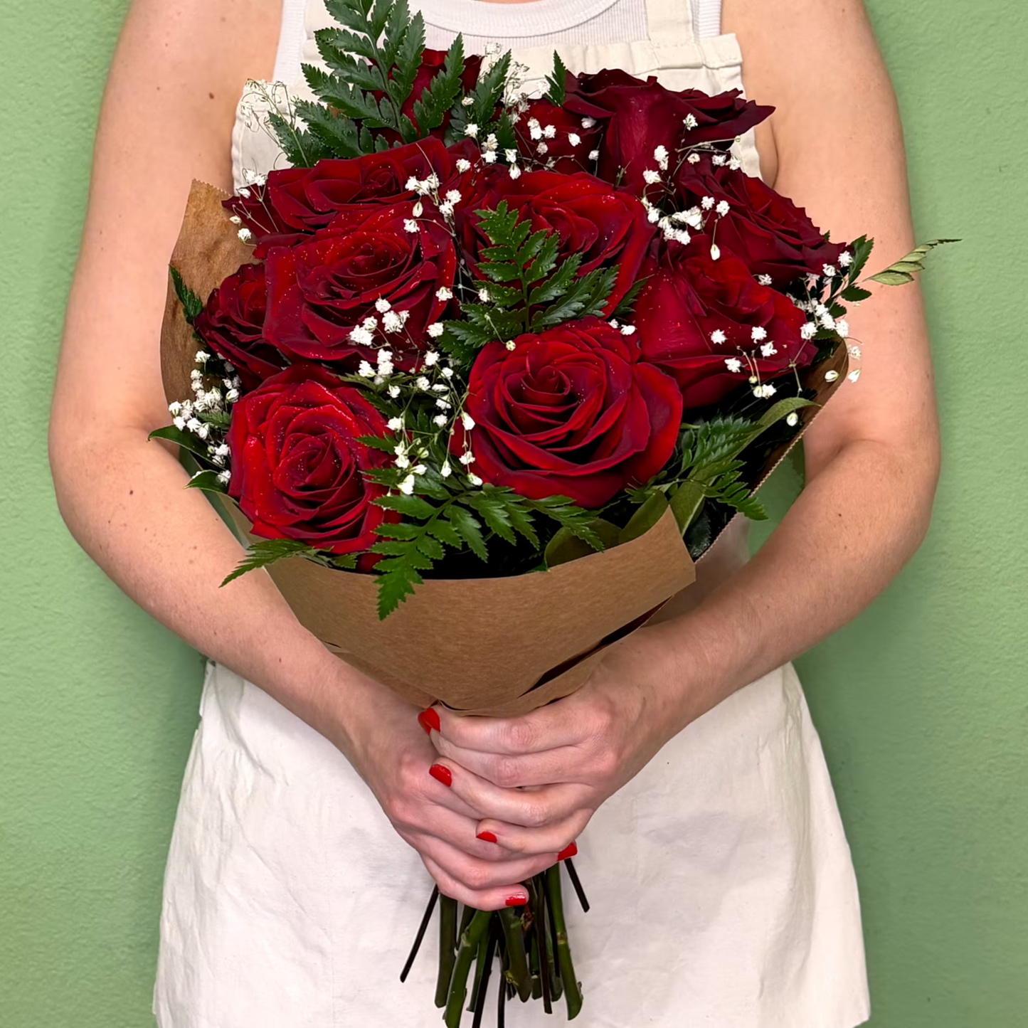 Person holding a bouquet of red roses against a green background