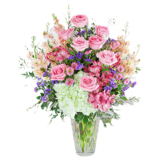 A floral arrangement featuring a variety of pink, purple, and white flowers with green foliage, arranged in a clear glass vase.