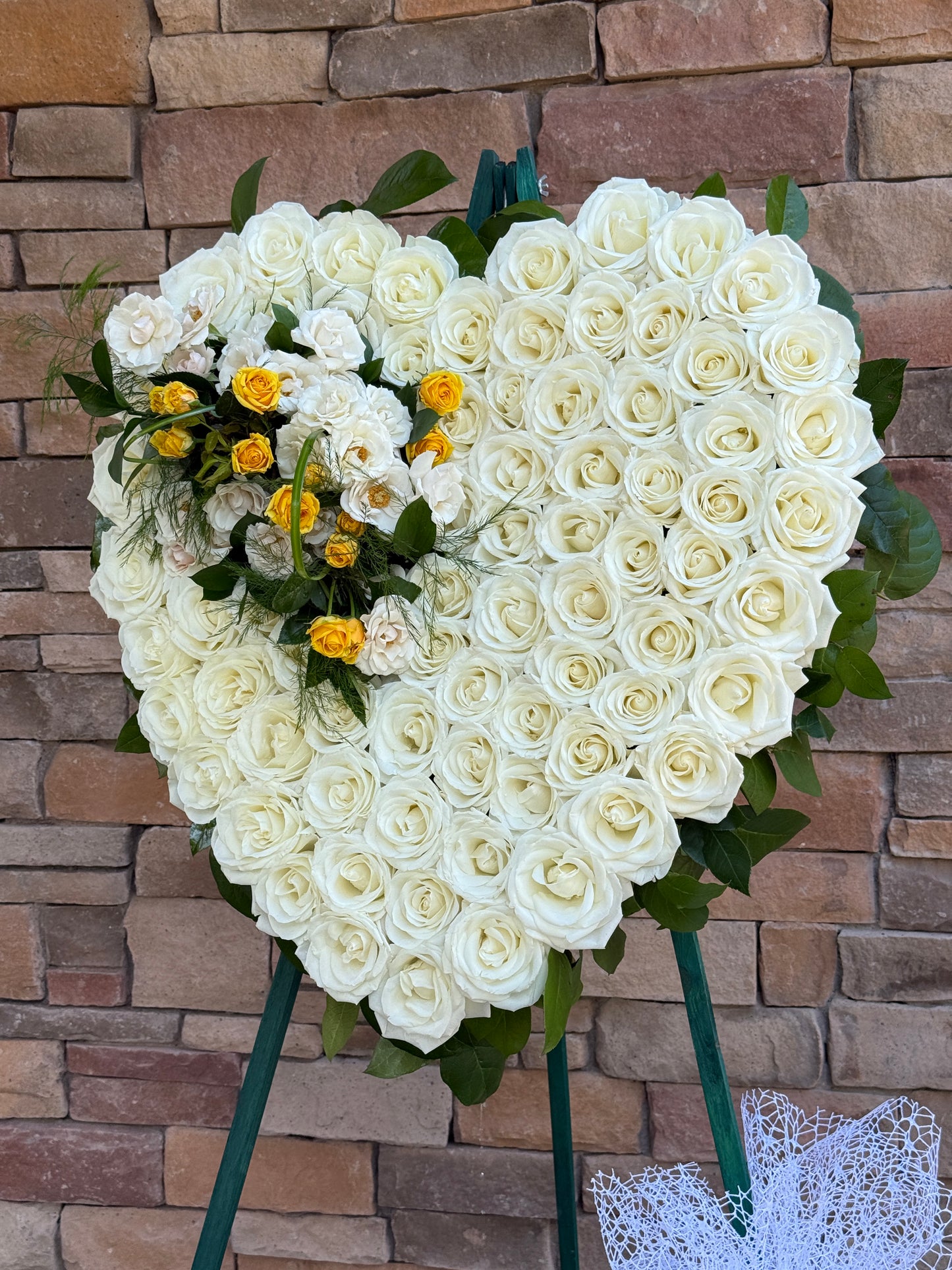 A large heart-shaped floral arrangement made of many white roses with green leaves, plus a smaller cluster of white and yellow roses. Delivered in Gilbert, Chandler, Queen Creek, Mesa, Tempe