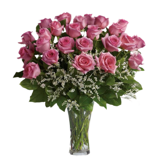 A clear glass vase containing a dozen pink roses with green leaves and decorative foliage.