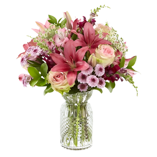 A pink floral bouquet featuring a variety of flowers such as pink roses, lilies, and greenery, arranged in a clear glass vase.