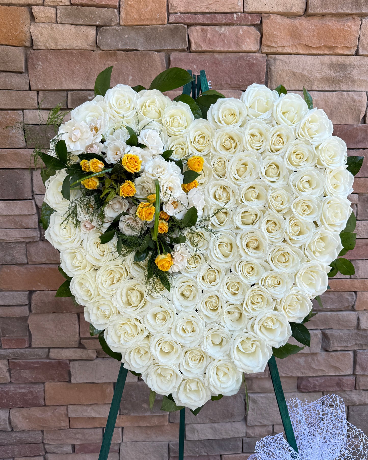 Heart-shaped floral arrangement made of white roses with small yellow roses and green foliage. FUNERAL FLOWERS delivered in Gilbert, Chandler, Mesa, Tempe, Queen creek, Phoenix